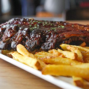 Costillas de cerdo BBQ con patatas fritas rústicas.