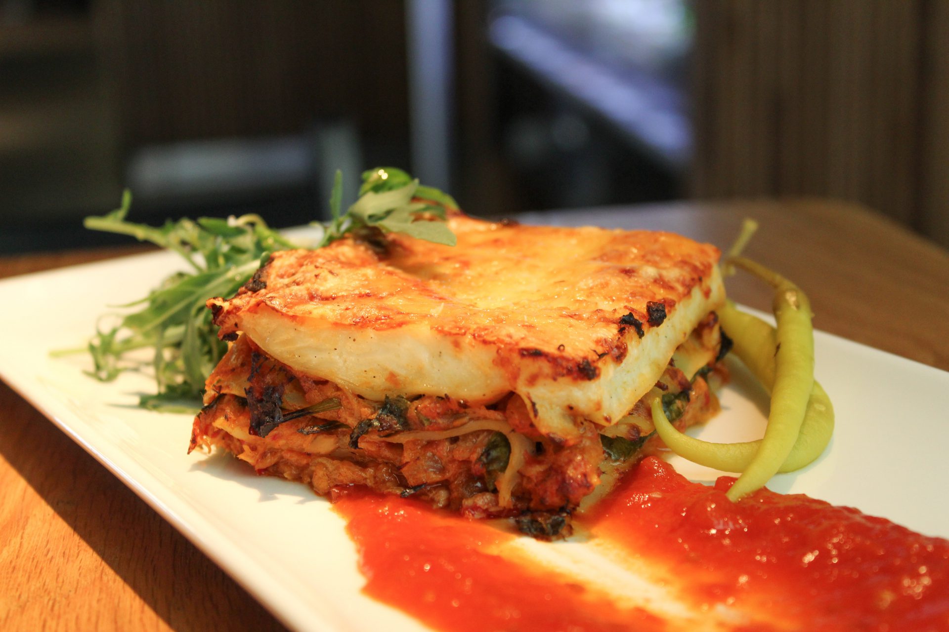 Lasaña de bonito con huevo y piparras con salsa de tomate y brotes verdes